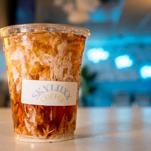 Iced coffee with cream swirls in a clear cup with a "Skyluxx Coffee" label on a counter.
