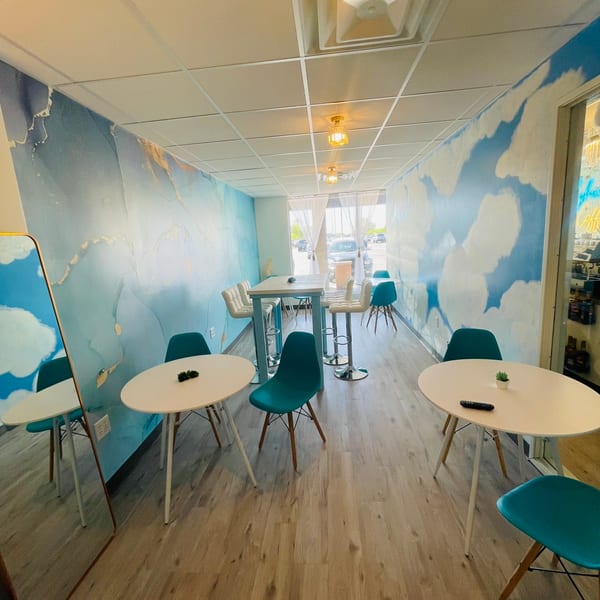 A cafe interior with light blue and gold abstract wall murals, white tables, and teal chairs.