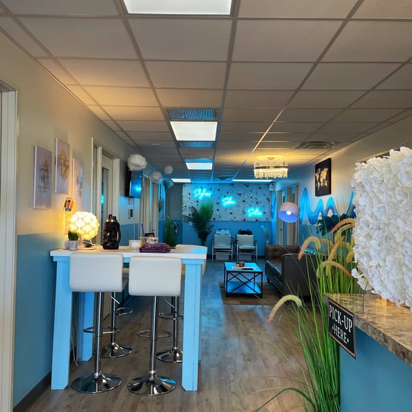 A modern salon interior with blue walls, neon signs, high-top tables, and a lounge area.