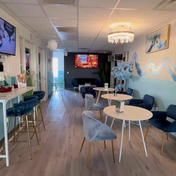 Modern cafe interior with blue and gold accents, featuring bar seating, small tables, and a lounge area.