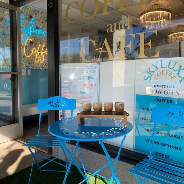 Skyluxx Coffee and Cafe storefront with blue outdoor seating and coffee samples on a table.
